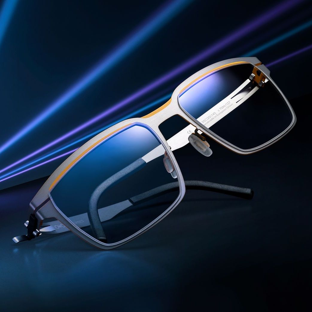 A pair of OVVO glasses in dark blue and yellow metal in front of a bright light-streaked background.