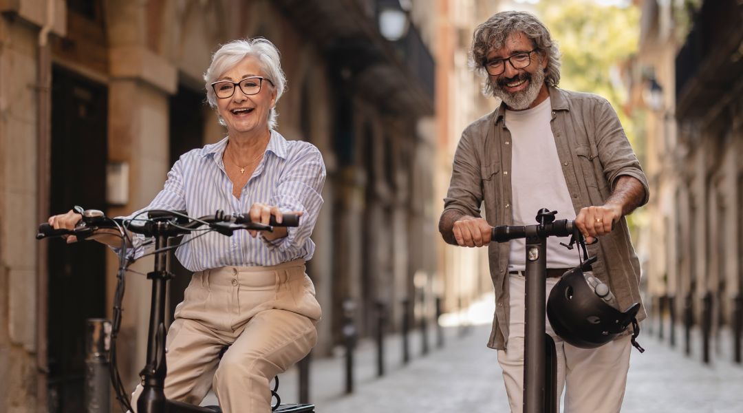A senior man and woman riding scooters and bicycles on a city street