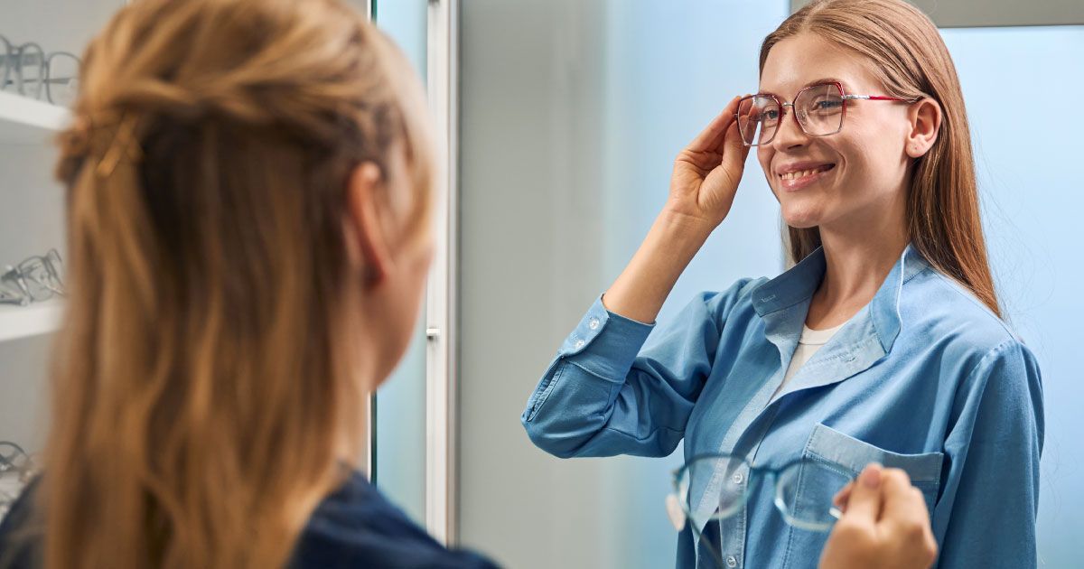 A woman is trying on glasses in front of an optician