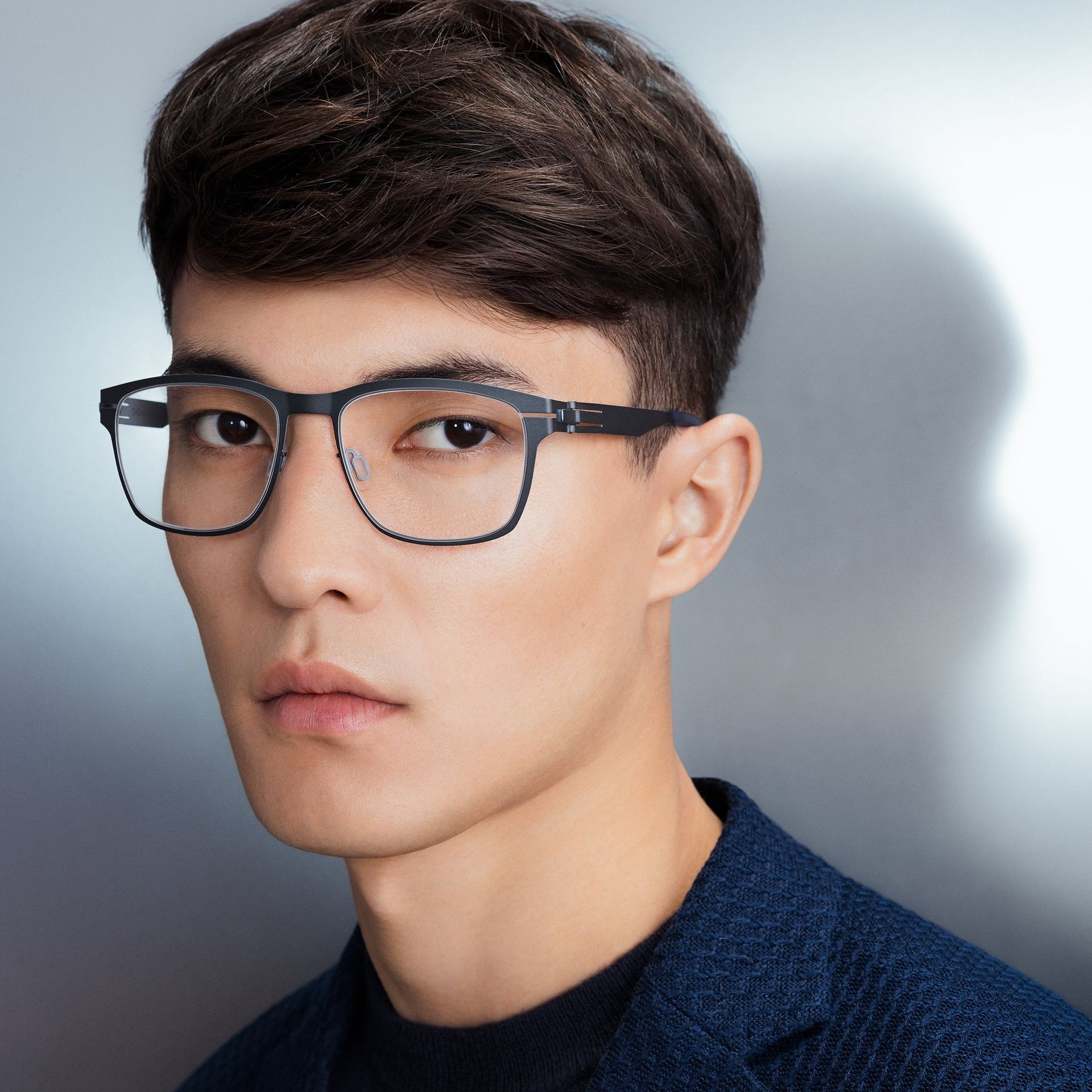 A young man wearing blue metal glasses and a blue jacket