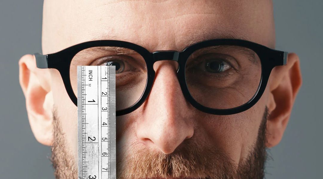A man wearing glasses holding a ruler in front of hisright eye .