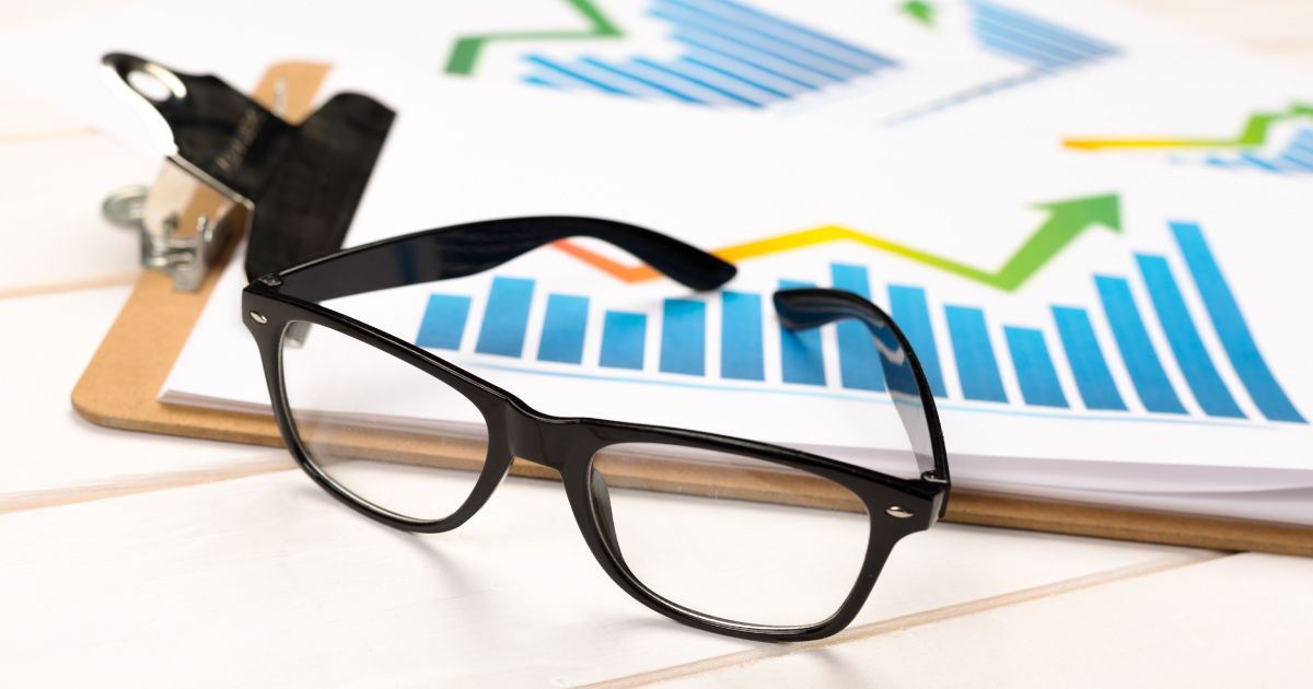 A pair of glasses is sitting on top of a clipboard with  a graph showing rising profits on it.