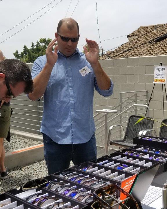Person in blue shirt trying on sunglasses at  Raise Your Glasses 2019 Event
