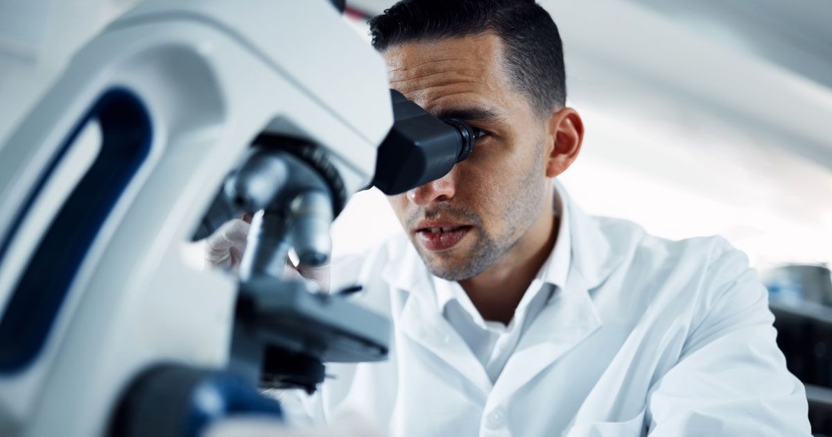 A man in a lab coat is looking through a microscope.