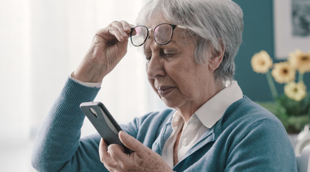 An elderly woman wearing glasses is looking at her cell phone .