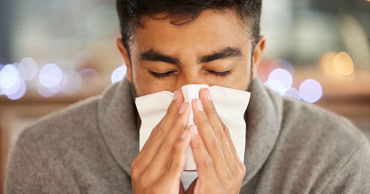 A man is blowing his nose into a facial napkin.