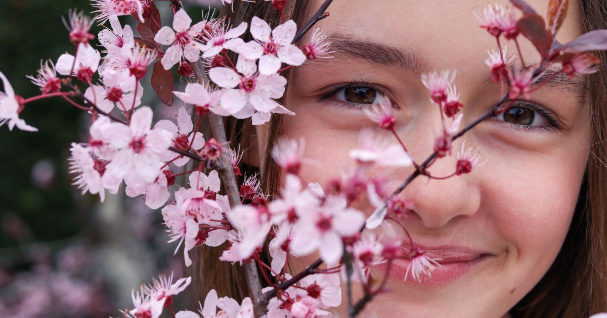 A young girl holding cherry blossoms in front of her face.