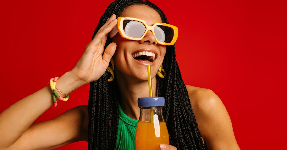 A woman wearing bright yellow sunglasses and bright accessories is happy and laughing.