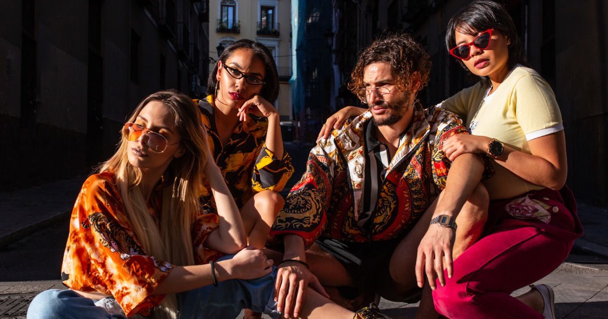 Four stylish friends posing outdoors in sunlight: two women on either side, one man in the center.