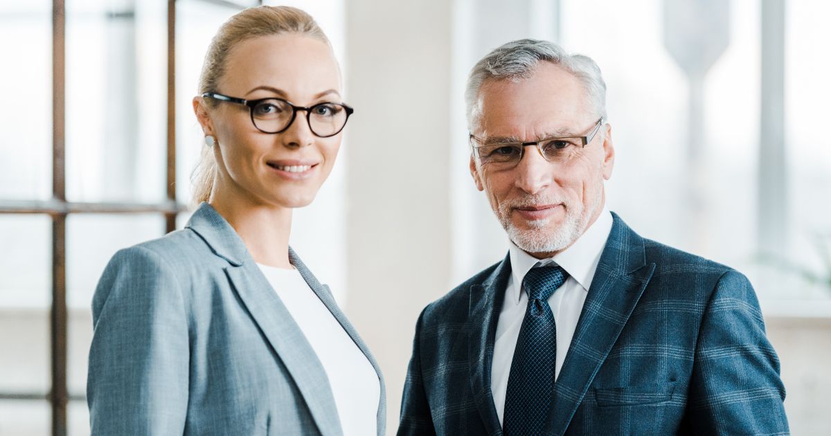 A man and a woman in business attire and luxury glasse are standing next to each other in an office.