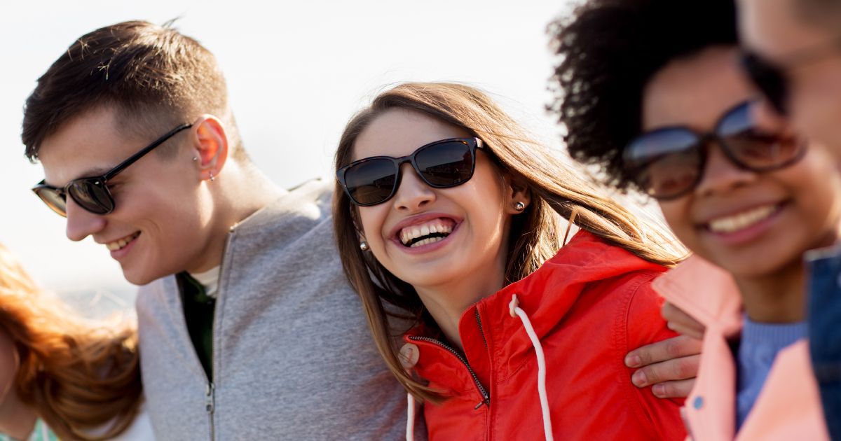 A group of young people wearing sunglasses are standing next to each other and smiling.