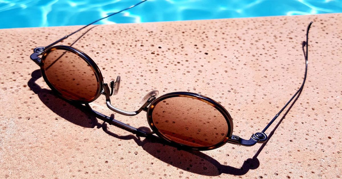 A pair of sunglasses is laying on the edge of a pool.