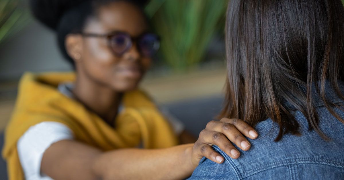 A woman has her hand on another woman 's shoulder.
