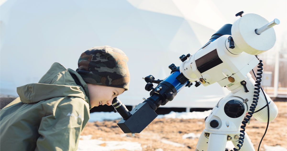 A young boy is looking through a telescope.