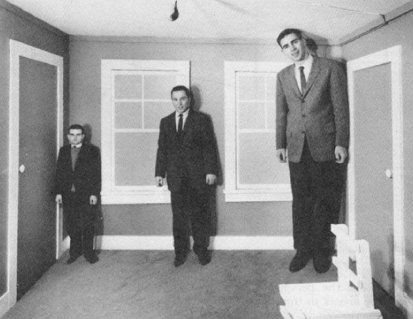 An example of the Ames Room illusion with black and white photo of three men standing in a room