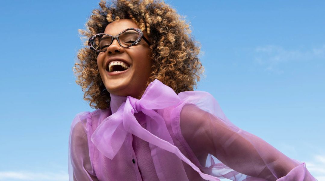 A woman wearing glasses and a purple shirt is laughing