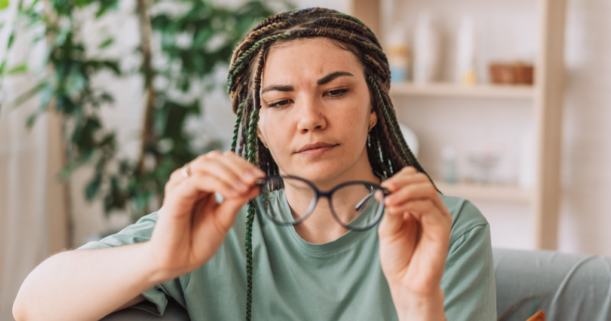 A woman is sitting on a couch holding a pair of glasses.