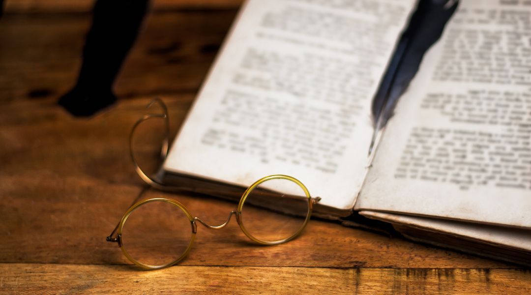 pair of vintage eyewear on a desk next to an old book with a feather on it.
