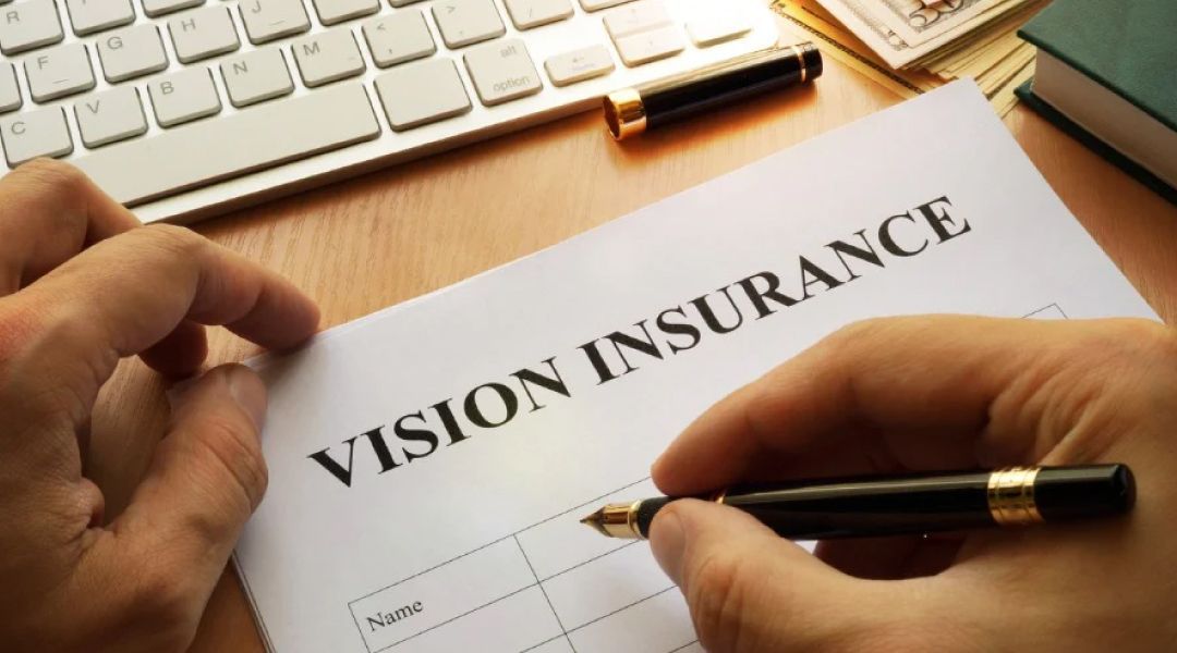 Person at a desk with a pen about to write on a form that says Vision Inurance