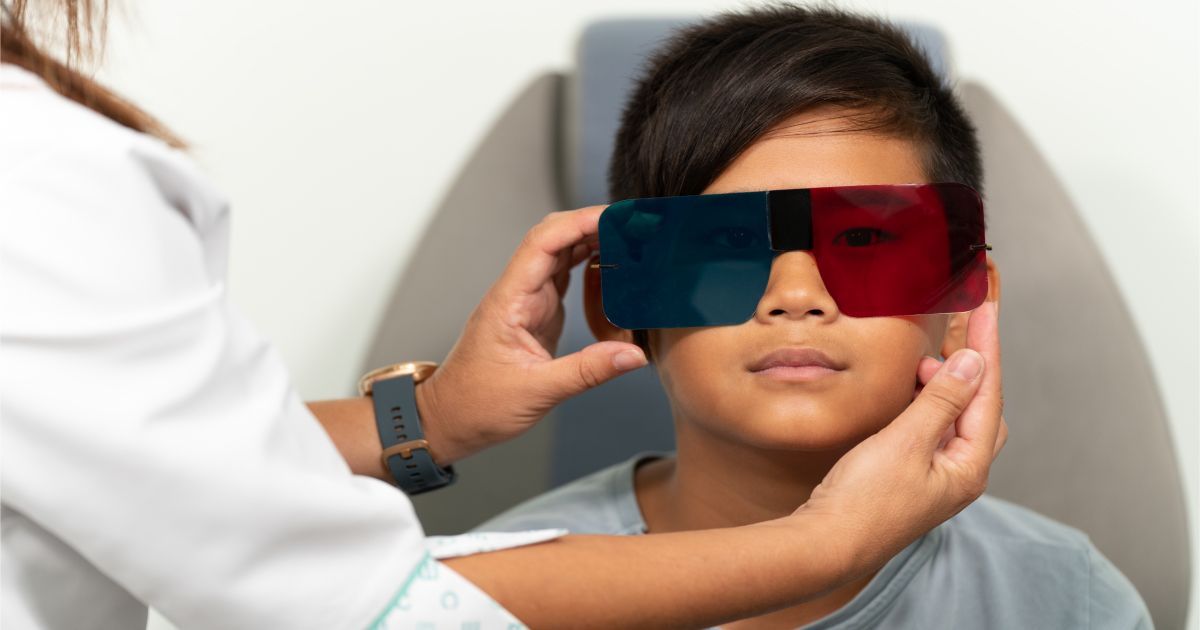 A young boy with glasses that have red and blue lenses is being seen by a vision therapist.