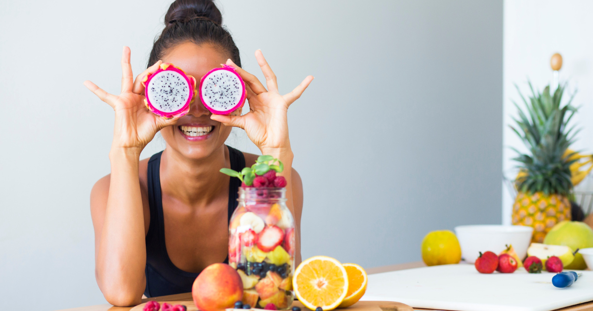 A woman sitting at a table with multiples is holding slices of dragon fruit in front of her eyes.