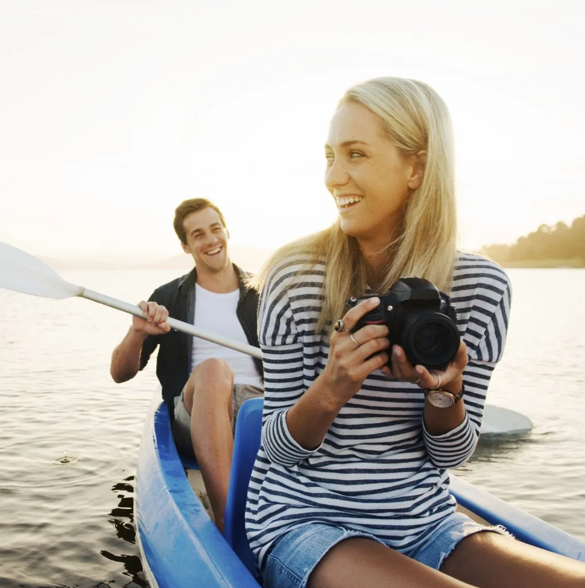 Woman with a camera and man with an oar in a canoe on lake during sunset