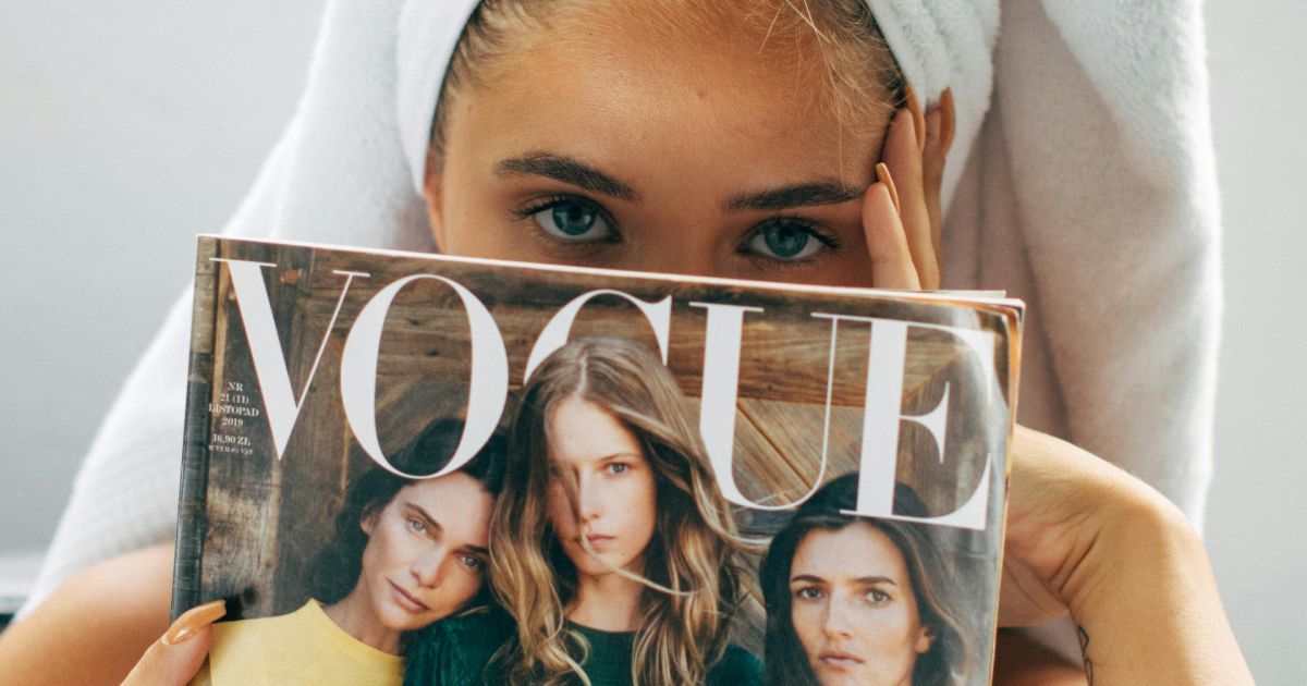 A woman with a towel wrapped around her head is holding a vogue magazine.