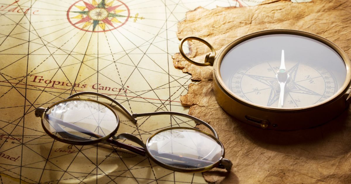 A pair of old glasses and a compass are sitting on top of an old map.