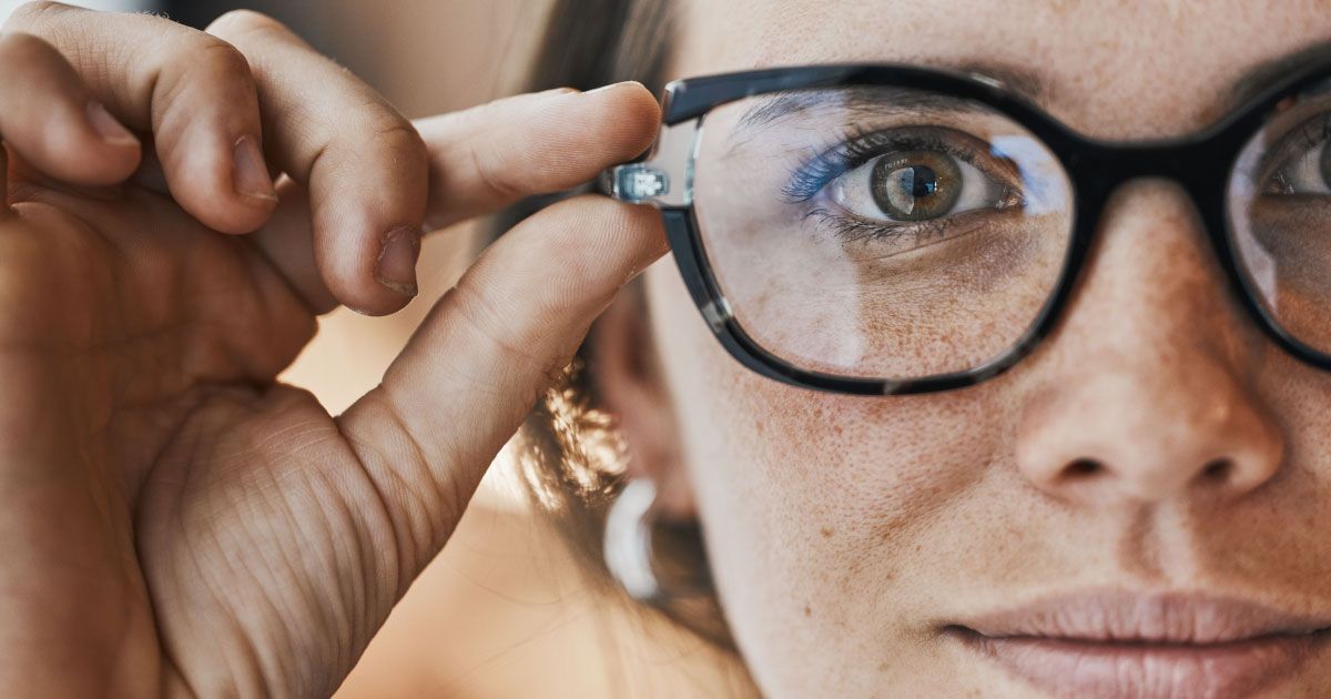 A close-up of a woman wearing glasses with her fingers on the right temple