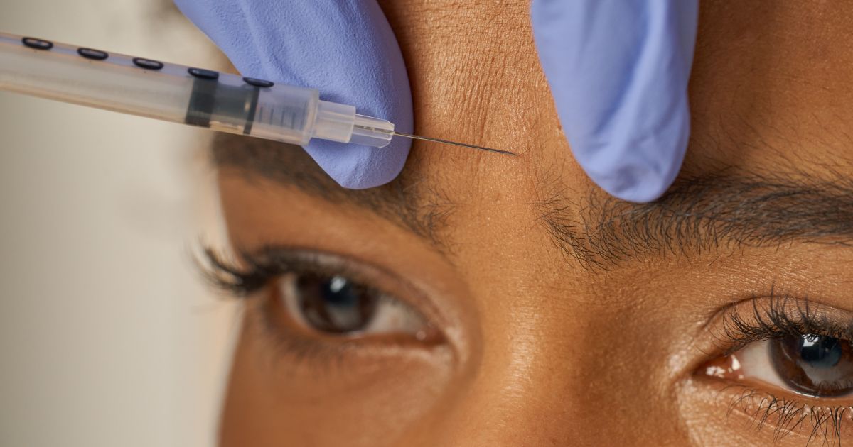 A person receiving an injection in their forehead; syringe held by a gloved hand.