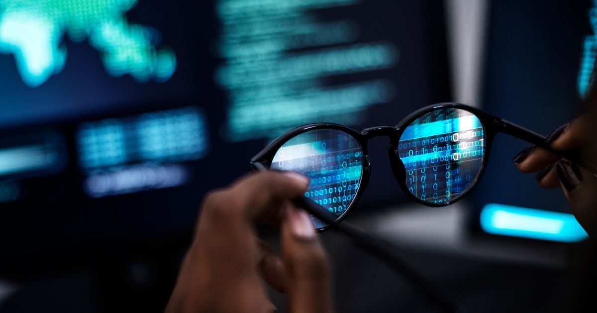 Person holding glasses reflecting a computer screen with code.