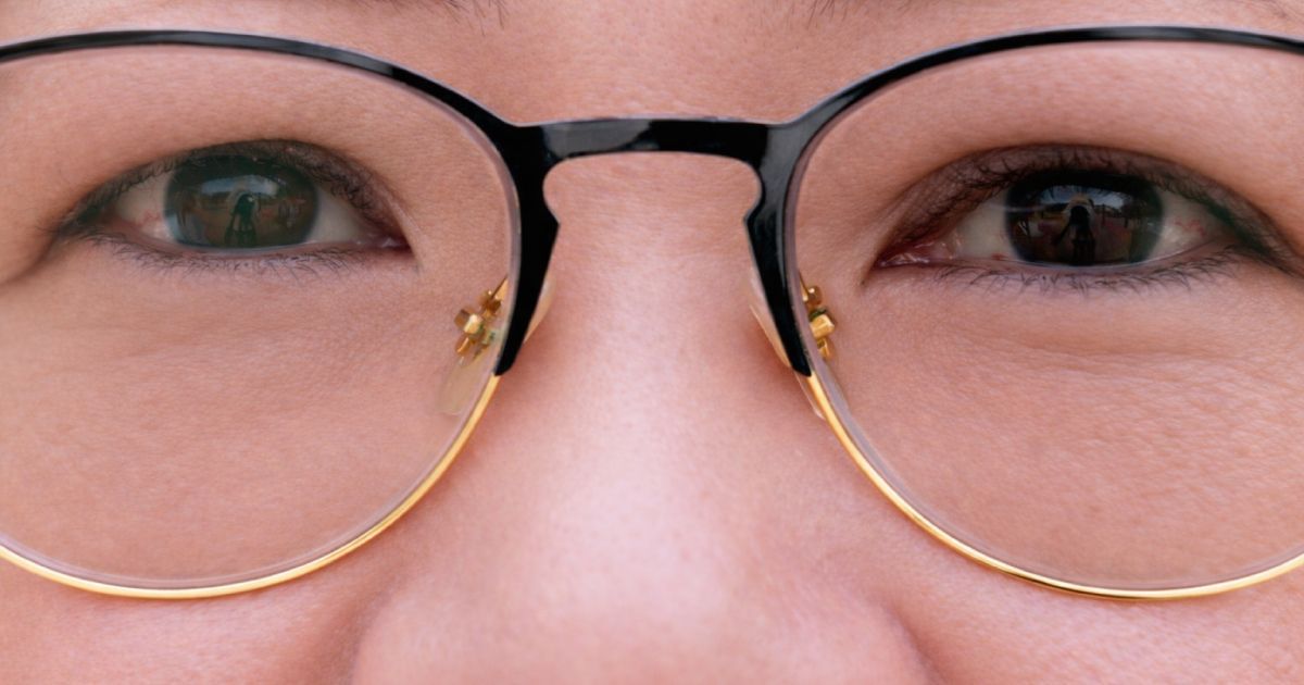 Close-up of a person's face wearing glasses with a black top rim and gold-colored rims; eyes looking forward.