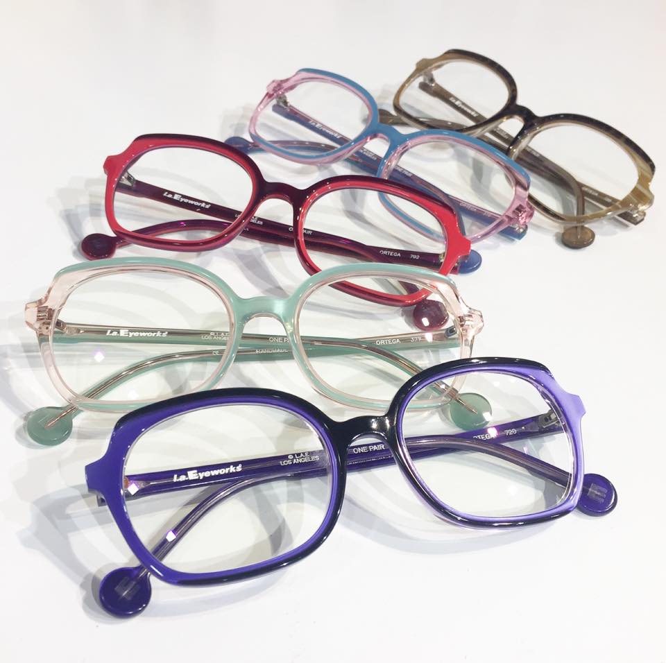 Five la Eyeworks frames in reds, purple, pink and neutral colors fanned out and layered over each other