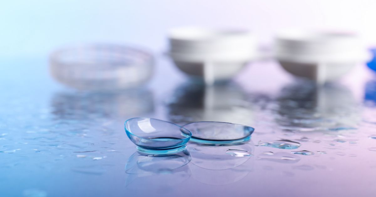 Two contact lenses with storage cases on a wet, light blue surface.