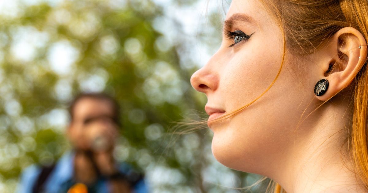 Woman in profile view looking off in the distance, with a blurred person in the background.