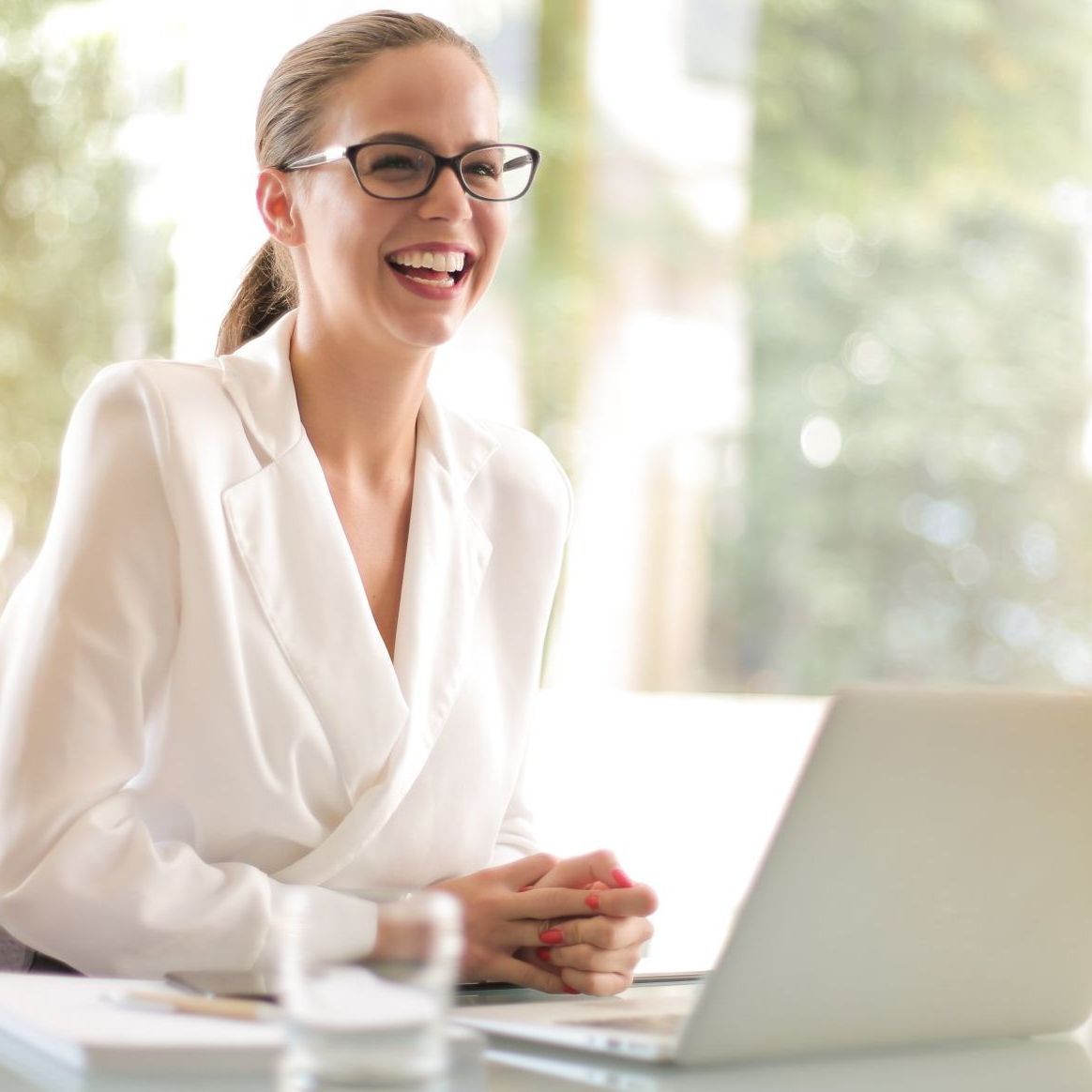 A woman wearing glasses sits at a desk with a laptop