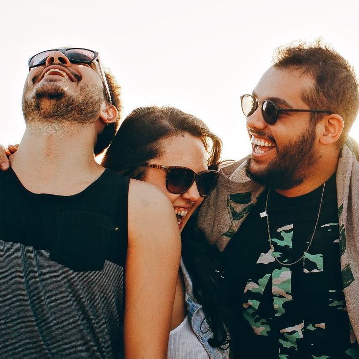 Two men and a woman wearing sunglasses are laughing together