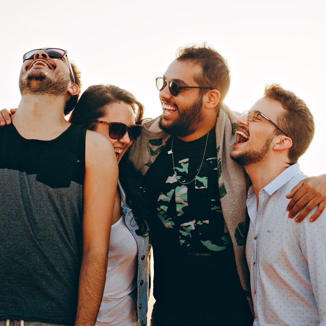 Four people wearing sun glasses in a group laughing