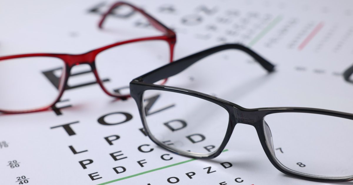 Two pairs of eyeglasses, red and black frames, on top of a Snellen eye chart.