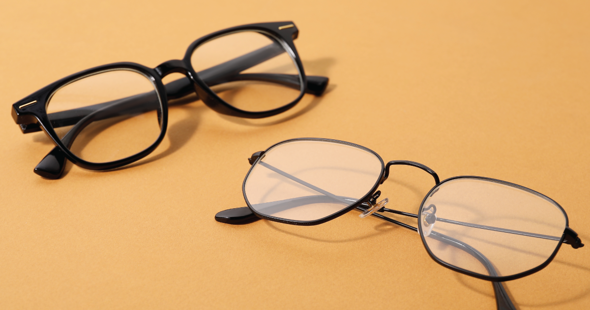 Two pairs of eyeglasses on a warm orange surface, one black and one thin metal frame