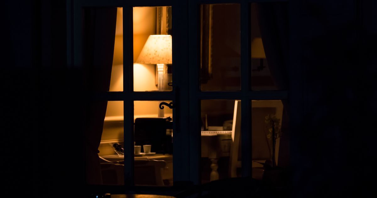 A view of a living room through a window with a lamp illuminated at night.