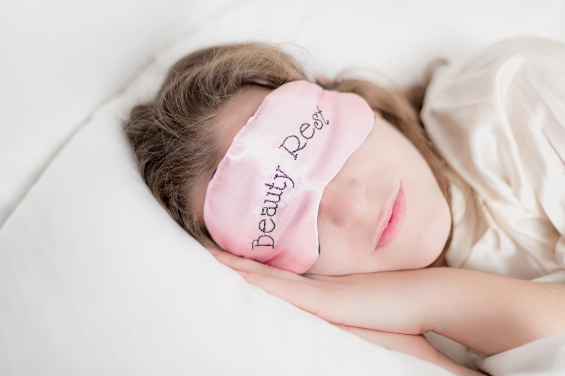 Woman with head on pillow wearing pink eye mask with Beauty Rest written on it
