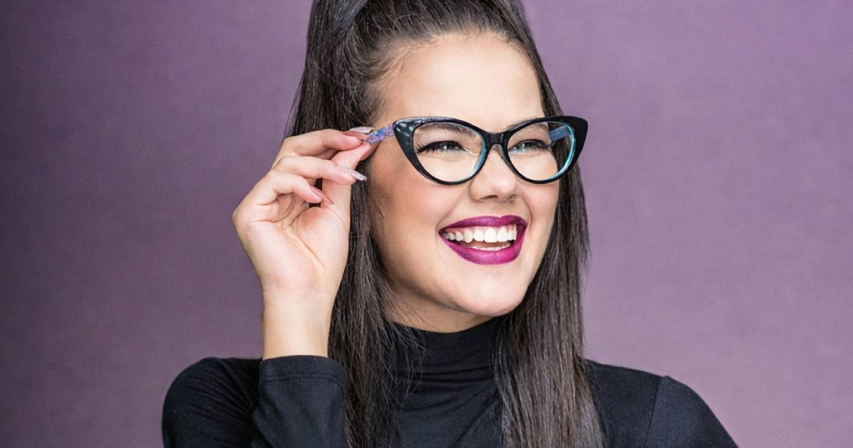 Woman with cat-eye glasses, smiling, touching frame. Purple background.
