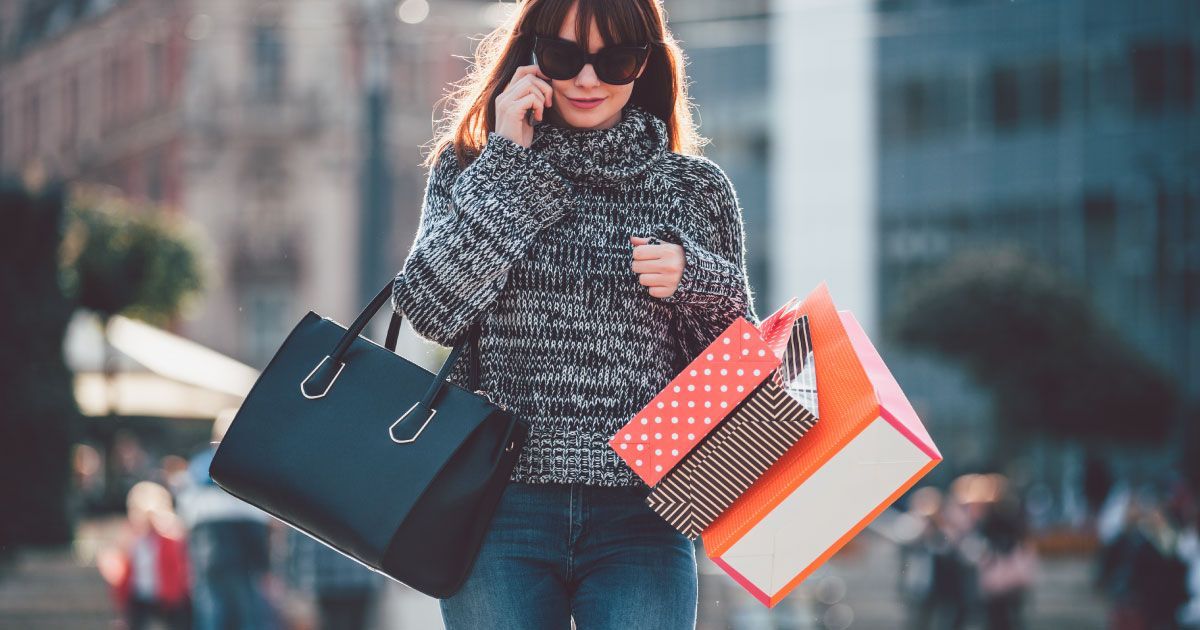 A woman is holding shopping bags and talking on a cell phone.