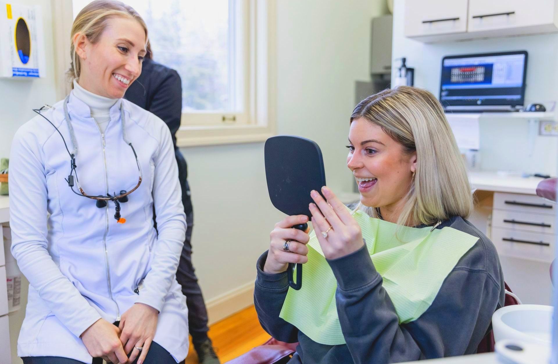 A woman is looking at her teeth in a mirror at the dentist.