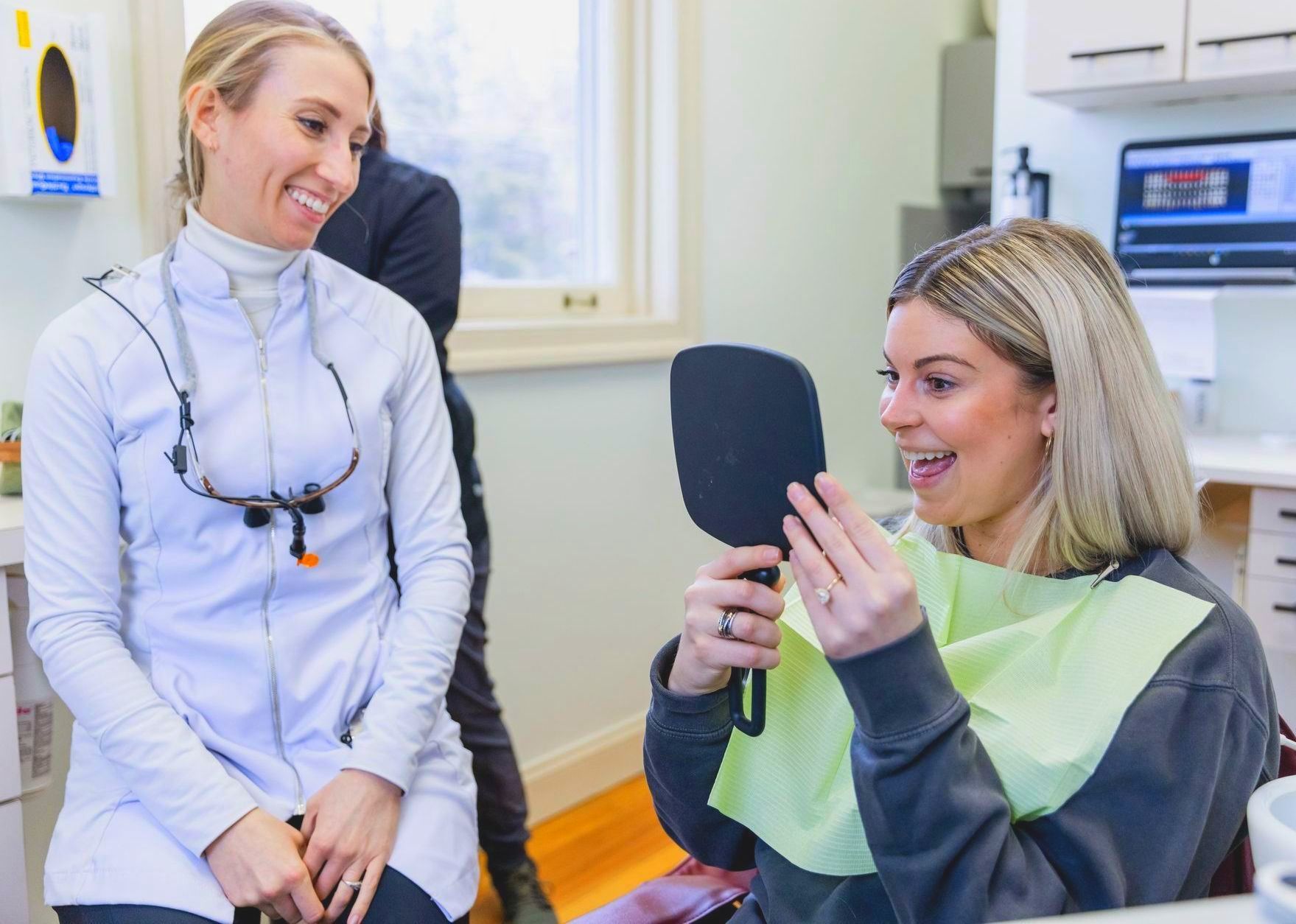 A woman is looking at her teeth in a mirror at the dentist.