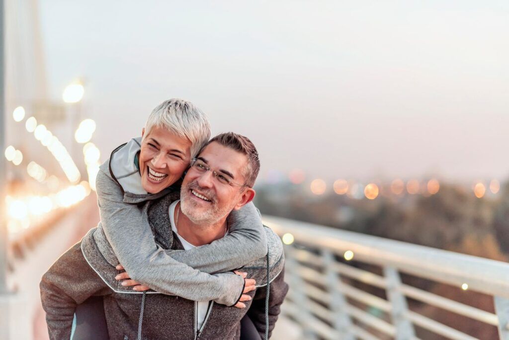 A man is giving a woman a piggyback ride on a bridge.