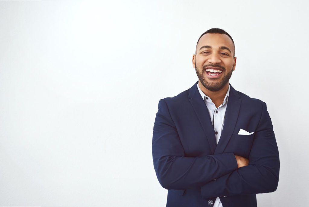 A man in a suit is standing with his arms crossed and smiling.