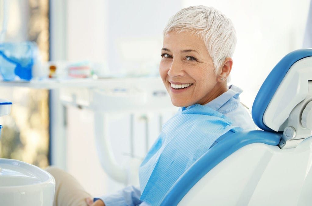 A woman is smiling while sitting in a dental chair.