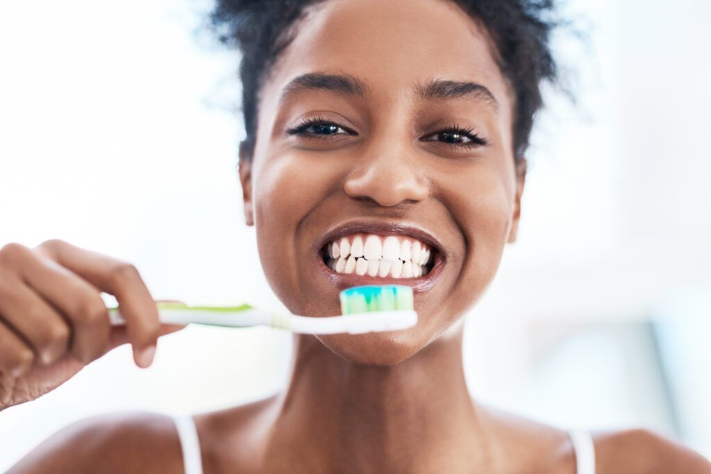 A woman is brushing her teeth with a toothbrush and smiling.